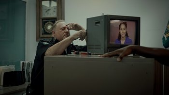 Movie still from “Amityville Uprising” (2022), directed by Thomas J. Churchill – A man sitting in front of a television; Medium shot, Over the shoulder angle