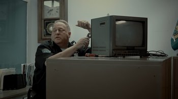 Movie still from “Amityville Uprising” (2022), directed by Thomas J. Churchill – A man sitting in front of a computer monitor; Medium shot, Low angle