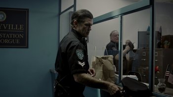 Movie still from “Amityville Uprising” (2022), directed by Thomas J. Churchill – A man in a police uniform is holding a bag; Medium shot, Over the shoulder angle