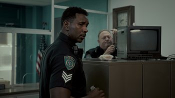Movie still from “Amityville Uprising” (2022), directed by Thomas J. Churchill – A police officer sitting in front of another officer; Medium shot, Over the shoulder angle