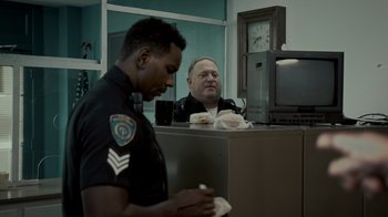 Movie still from “Amityville Uprising” (2022), directed by Thomas J. Churchill – A police officer is looking at a man sitting in front of a desk; Medium shot, Over the shoulder angle