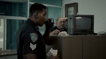 Movie still from “Amityville Uprising” (2022), directed by Thomas J. Churchill – A police officer is drinking from a cup; Medium shot, Over the shoulder angle