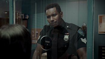 Movie still from “Amityville Uprising” (2022), directed by Thomas J. Churchill – A police officer looking out of a glass window; Close Up shot, Over the shoulder angle
