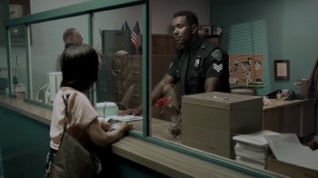Movie still from “Amityville Uprising” (2022), directed by Thomas J. Churchill – A police officer is talking to a woman in front of a store window; Medium shot, Over the shoulder angle