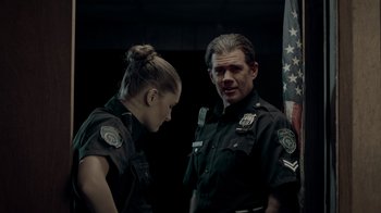 Movie still from “Amityville Uprising” (2022), directed by Thomas J. Churchill – A man and a woman in police uniforms standing next to each other; Medium shot, Low angle