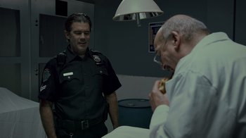 Movie still from “Amityville Uprising” (2022), directed by Thomas J. Churchill – A police officer and an older man eating a sandwich; Medium shot, Over the shoulder angle