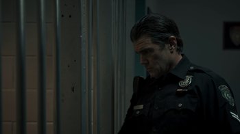 Movie still from “Amityville Uprising” (2022), directed by Thomas J. Churchill – A man in a police uniform is looking down; Medium shot, Over the shoulder angle