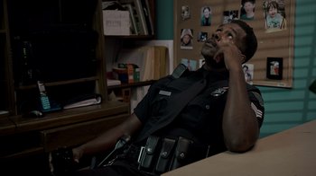 Movie still from “Amityville Uprising” (2022), directed by Thomas J. Churchill – A police officer sitting in a chair talking on a phone; Medium shot, High angle