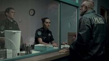 Movie still from “Amityville Uprising” (2022), directed by Thomas J. Churchill – A police officer sitting at a desk in front of a mirror; Medium shot, Over the shoulder angle