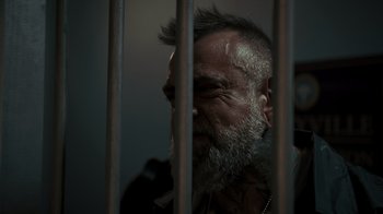 Movie still from “Amityville Uprising” (2022), directed by Thomas J. Churchill – An old man with a beard is behind bars; Close Up shot, Low angle