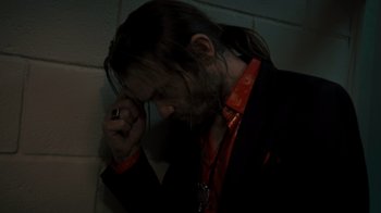 Movie still from “Amityville Uprising” (2022), directed by Thomas J. Churchill – A man with long black hair wearing a black jacket and a red tie; Close Up shot, High angle