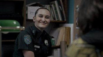 Movie still from “Amityville Uprising” (2022), directed by Thomas J. Churchill – A police officer smiling for the camera in her office; Close Up shot, Over the shoulder angle