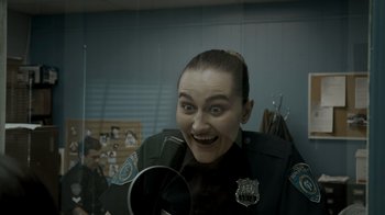 Movie still from “Amityville Uprising” (2022), directed by Thomas J. Churchill – A woman in a police officer's uniform is smiling for the camera; Close Up shot, Over the shoulder angle