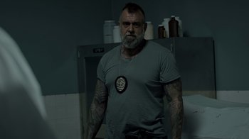 Movie still from “Amityville Uprising” (2022), directed by Thomas J. Churchill – A man with a beard and tattoos standing in a kitchen; Medium shot, Over the shoulder angle