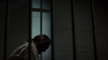 Movie still from “Amityville Uprising” (2022), directed by Thomas J. Churchill – A man in a jail cell with his head down; Medium shot, High angle