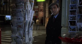 Movie still from “An American Werewolf in Paris” (1997), directed by Anthony Waller – A man smoking a cigarette while standing next to newspapers; Medium shot, Low angle