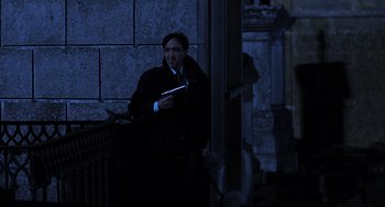 Movie still from “An American Werewolf in Paris” (1997), directed by Anthony Waller – A man standing in the dark holding a book; Medium shot, Low angle