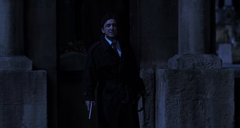 Movie still from “An American Werewolf in Paris” (1997), directed by Anthony Waller – A man in a trench coat holding a gun in the dark; Medium shot, Low angle