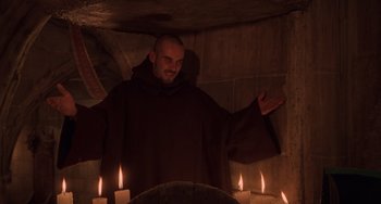 Movie still from “An American Werewolf in Paris” (1997), directed by Anthony Waller – A man wearing a monk's robe standing in front of candles; Medium shot, Low angle