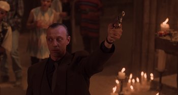 Movie still from “An American Werewolf in Paris” (1997), directed by Anthony Waller – A man in a suit holding a gun in front of candles; Medium shot, Low angle