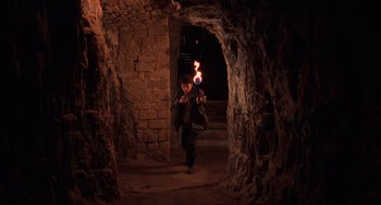 Movie still from “An American Werewolf in Paris” (1997), directed by Anthony Waller – A man is holding a torch in a cave; Wide shot, High angle