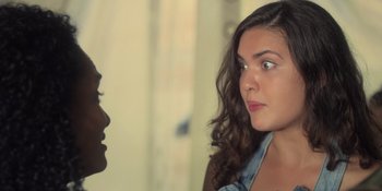 Movie still from “An Unforgettable Year: Summer” (2023), directed by Cris D'Amato – A woman with long curly hair is looking at another woman with long curly hair; Close Up shot, Over the shoulder angle