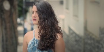 Movie still from “An Unforgettable Year: Summer” (2023), directed by Cris D'Amato – A beautiful woman with long , curly hair standing outside; Close Up shot, Low angle
