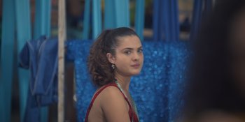 Movie still from “An Unforgettable Year: Summer” (2023), directed by Cris D'Amato – A young woman in a red dress is looking at the camera; Close Up shot, Over the shoulder angle