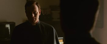 Movie still from “Angels & Demons” (2009), directed by Ron Howard – A man wearing a priest's outfit standing in front of a window; Close Up shot, Over the shoulder angle