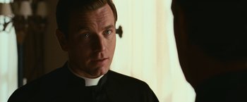 Movie still from “Angels & Demons” (2009), directed by Ron Howard – A man wearing a priest's outfit looking at the camera; Close Up shot, Over the shoulder angle