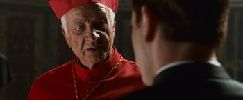 Movie still from “Angels & Demons” (2009), directed by Ron Howard – A man wearing a red hat talking to another man wearing a suit; Close Up shot, Over the shoulder angle
