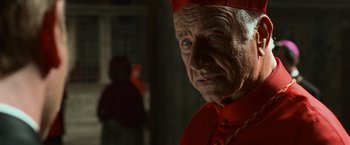 Movie still from “Angels & Demons” (2009), directed by Ron Howard – An older man in a red outfit looking at the camera; Close Up shot, Over the shoulder angle