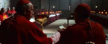 Movie still from “Angels & Demons” (2009), directed by Ron Howard – A priest sitting in front of a large group of people; Medium shot, Over the shoulder angle