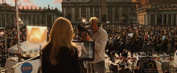 Movie still from “Angels & Demons” (2009), directed by Ron Howard – A man is filming a woman in front of a crowd; Medium shot, Over the shoulder angle