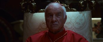 Movie still from “Angels & Demons” (2009), directed by Ron Howard – An older man wearing a red shirt and a gold chain around his neck; Close Up shot, Low angle