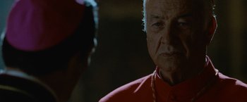 Movie still from “Angels & Demons” (2009), directed by Ron Howard – An older man wearing a red shirt looking at the camera; Close Up shot, Over the shoulder angle