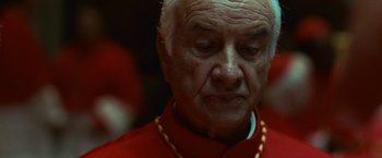 Movie still from “Angels & Demons” (2009), directed by Ron Howard – An older man in a red shirt and a yellow necklace; Close Up shot, Low angle