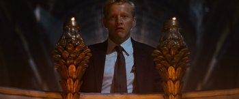 Movie still from “Angels & Demons” (2009), directed by Ron Howard – A man wearing a suit and tie standing in front of a chair; Medium shot, Low angle