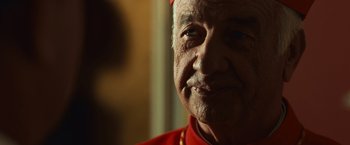 Movie still from “Angels & Demons” (2009), directed by Ron Howard – An older man in a red shirt is looking at the camera; Close Up shot, Over the shoulder angle