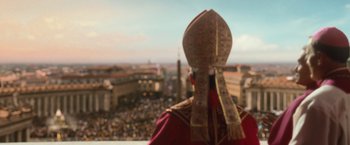 Movie still from “Angels & Demons” (2009), directed by Ron Howard – A man in a red and gold outfit is looking out over a city; Medium shot, Over the shoulder angle