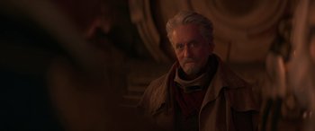 Movie still from “Ant-Man and the Wasp: Quantumania” (2023), directed by Peyton Reed – An older man with a gray beard wearing a red scarf; Close Up shot, Over the shoulder angle