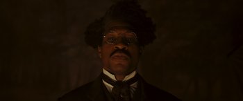 Movie still from “Ant-Man and the Wasp: Quantumania” (2023), directed by Peyton Reed – A man in a suit and tie wearing a wig; Close Up shot, Low angle