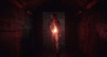 Movie still from “Antlers” (2021), directed by Scott Cooper – A man standing in a dark hallway holding a flashlight; Wide shot, Low angle