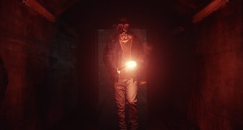 Movie still from “Antlers” (2021), directed by Scott Cooper – A man wearing a gas mask and holding a light; Medium shot, Low angle