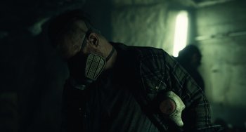 Movie still from “Antlers” (2021), directed by Scott Cooper – A man wearing a gas mask and a plaid shirt; Close Up shot, Over the shoulder angle