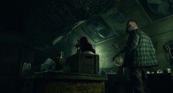 Movie still from “Antlers” (2021), directed by Scott Cooper – A man standing next to a table in a dark room; Wide shot, Low angle