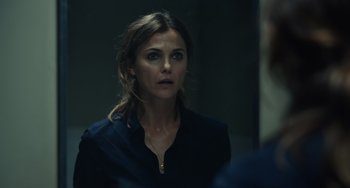Movie still from “Antlers” (2021), directed by Scott Cooper – A woman in a black shirt is looking at her reflection in a mirror; Close Up shot, Over the shoulder angle