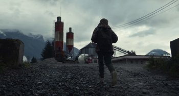 Movie still from “Antlers” (2021), directed by Scott Cooper – A person walking in front of a cement factory; Extreme Wide shot, Low angle