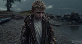 Movie still from “Antlers” (2021), directed by Scott Cooper – A young boy wearing a camo jacket and looking sad; Medium shot, High angle
