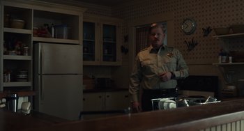 Movie still from “Antlers” (2021), directed by Scott Cooper – A man standing in a kitchen next to a refrigerator; Medium shot, Over the shoulder angle